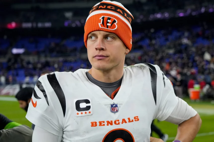 FootballR - NFL - Cincinnati Bengals Quarterback Joe Burrow in orange-weißer Uniform steht auf einem Feld.
