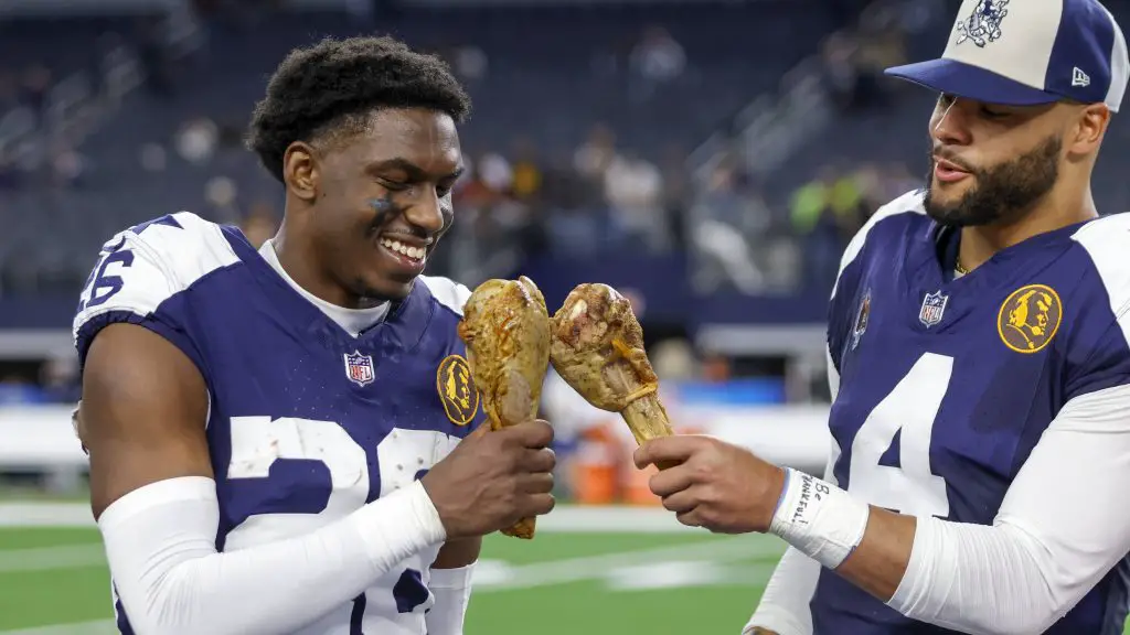 FootballR - NFL Thanksgiving Zuschauerrekord - DaRon Bland und Dak Prescott halten Truthahnkeulen auf einem Feld und erinnern sich dabei an die Geschichte, die durch den aufregenden Pick-6 geschrieben wurde.