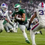 FootballR - NFL - Der Eagles QB Jalen Hurts läuft mit dem Ball auf einem Feld.