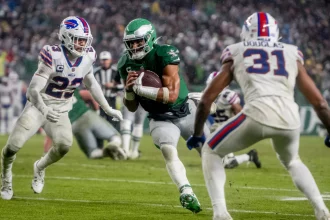 FootballR - NFL - Der Eagles QB Jalen Hurts läuft mit dem Ball auf einem Feld.