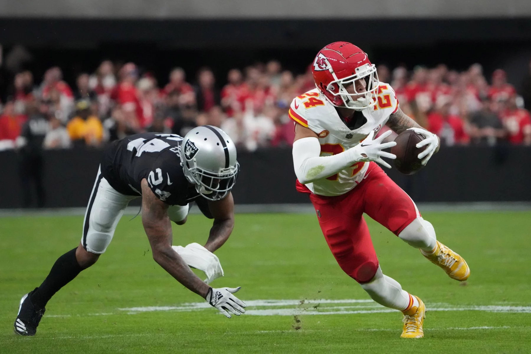 FootballR - NFL - ein Footballspieler der Kansas City Chiefs, weicht gekonnt der Verteidigung der Raiders, Marcus Peters, aus, indem er furchtlos mit dem Ball nach vorne prescht.