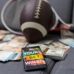 FootballR - NFL - Ein Mobiltelefon mit der Aufschrift NFL Wetten liegt auf einem Stapel Geld und einem Football.