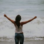 FootballR - NFL - Eine Frau steht mit ausgestreckten Armen am Strand.