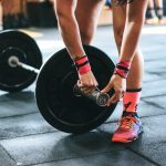 FootballR - NFL - Quarterback-Training - Eine Frau hebt in einem Fitnessstudio eine Langhantel.