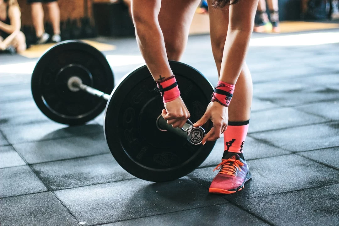 FootballR - NFL - Quarterback-Training - Eine Frau hebt in einem Fitnessstudio eine Langhantel.