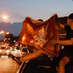 FootballR - NFL - Ein Mann hält nachts eine Flagge auf dem Dach eines Autos.