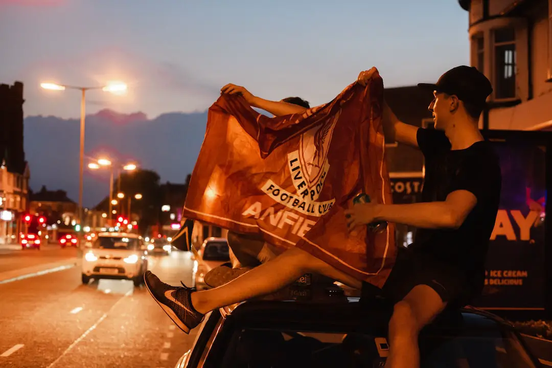 FootballR - NFL - Ein Mann hält nachts eine Flagge auf dem Dach eines Autos.