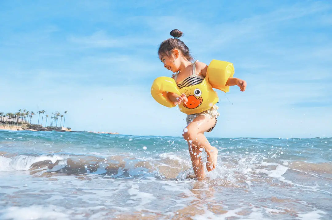 FootballR - NFL - Ein kleines Mädchen, das mit einer gelben Schwimmweste im Meer spielt.