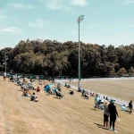 FootballR - NFL - Eine Gruppe von Menschen sitzt auf dem Rasen eines Baseballfeldes.