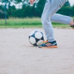 FootballR - NFL - Ein Junge kickt einen Fußball auf einem unbefestigten Feld.
