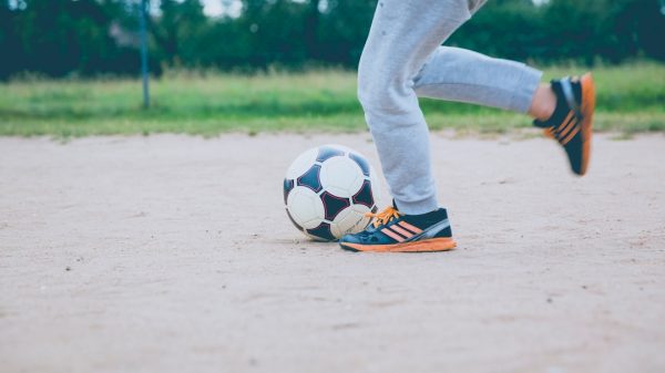 FootballR - NFL - Ein Junge kickt einen Fußball auf einem unbefestigten Feld.