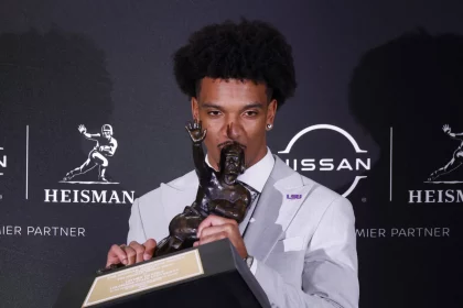 FootballR - NFL - Patriots vor Auswahl eines Quarterbacks - Jayden Daniels hält eine Trophäe vor einer Wand.