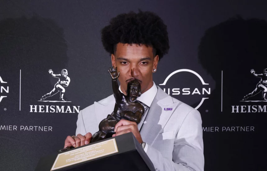 FootballR - NFL - Patriots vor Auswahl eines Quarterbacks - Jayden Daniels hält eine Trophäe vor einer Wand.