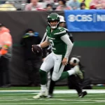 FootballR - NFL - Ein New Yorker Footballspieler in grüner Uniform, Zach Wilson, der mit einem Ball läuft und möglicherweise zum Spieler der Woche - Player of the Week - unter den QBs ernannt wurde.