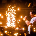 FootballR - NFL - Diese Beschreibung wurde automatisch generiert. DJ Tiësto mit einem Mikrofon auf der Bühne während des Super Bowl LVIII.