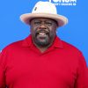 FootballR - NFL - Super Bowl Soulful Celebration 25th Anniversary - Diese Beschreibung wurde automatisch generiert. Ein Mann in rotem Hemd und Hut steht während des Super Bowl auf einem blauen Teppich.