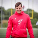 FootballR - NFL - Bernhard Seikovits steht mit einem roten Kapuzenpullover auf einem Footballfeld.