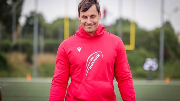 FootballR - NFL - Bernhard Seikovits steht mit einem roten Kapuzenpullover auf einem Footballfeld.