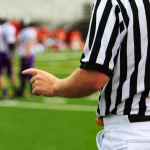 FootballR - NFL - Ein Schiedsrichter zeigt auf eine Fußballmannschaft auf dem Spielfeld.