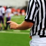 FootballR - NFL - Ein Schiedsrichter zeigt auf eine Fußballmannschaft auf dem Spielfeld.