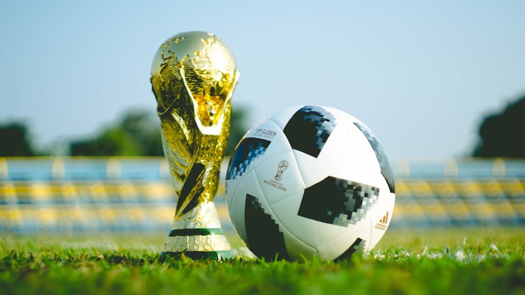 FootballR - NFL - Diese Beschreibung wurde automatisch generiert. Ein Fußball und eine Trophäe auf Gras.