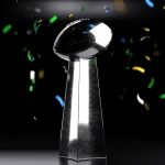 FootballR - NFL - Diese Beschreibung wurde automatisch generiert. Die Super Bowl-Trophäe ist von Konfetti umgeben.
Schlüsselwörter: Super Bowl