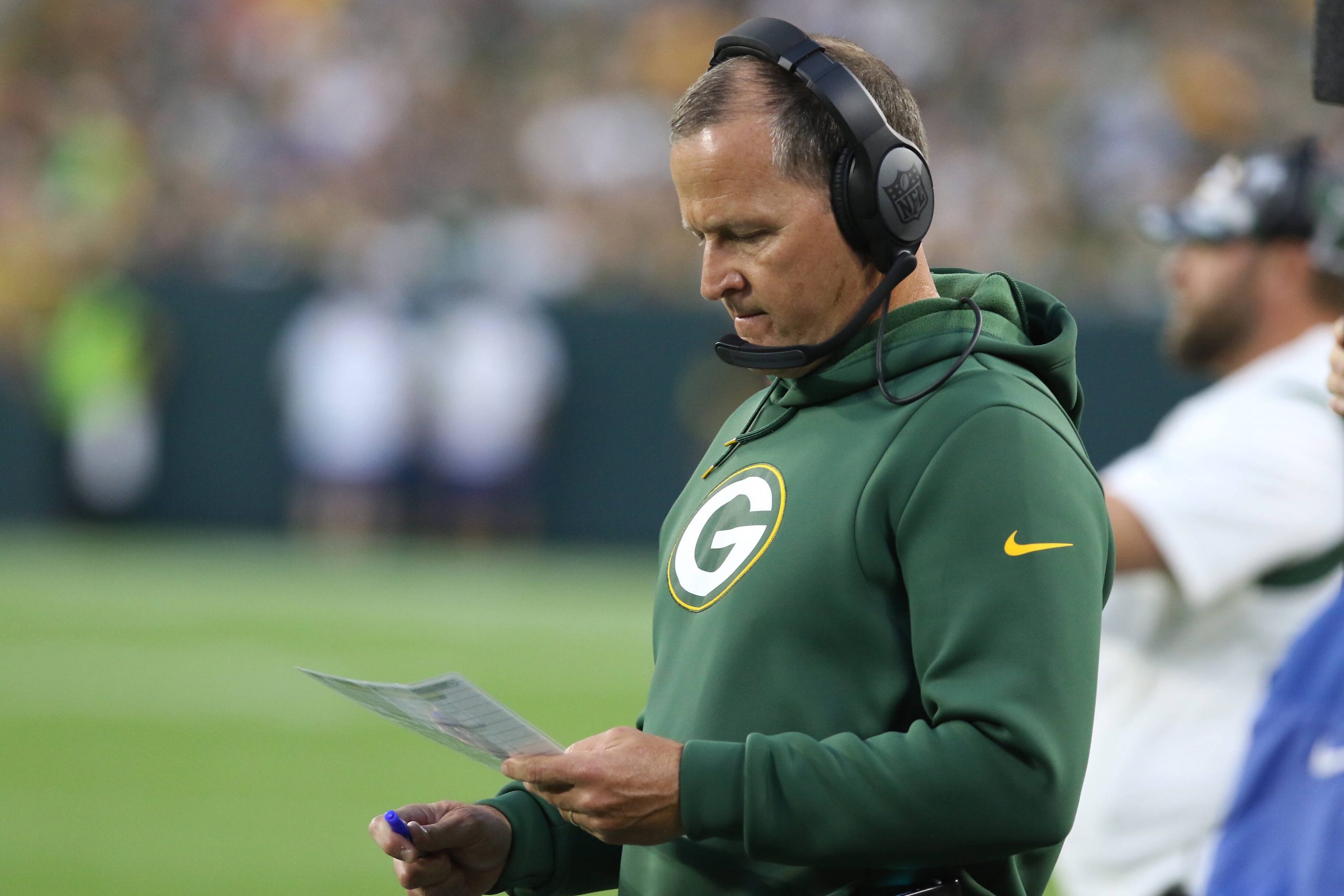 FootballR - NFL - Diese Beschreibung wurde automatisch generiert. Der Defensivkoordinator der Green Bay Packers, Joe Barry, blickt auf ein Blatt Papier.