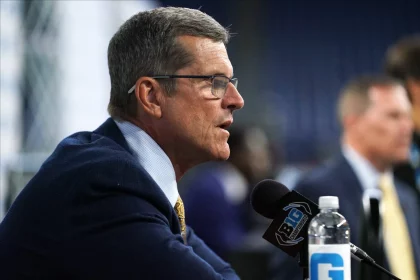 FootballR - NFL - Offseason-Programm - Diese Beschreibung wurde automatisch generiert. Ein Mann in Anzug und Krawatte, Jim Harbaugh, spricht in ein Mikrofon über die NFL und die Los Angeles Chargers.