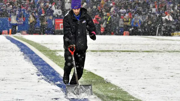 FootballR - NFL - Ein Helfer schaufelt Schnee auf dem Footballplatz im Highmark Stadium.