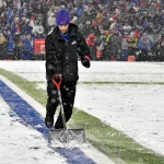 FootballR - NFL - Ein Helfer schaufelt Schnee auf dem Footballplatz im Highmark Stadium.