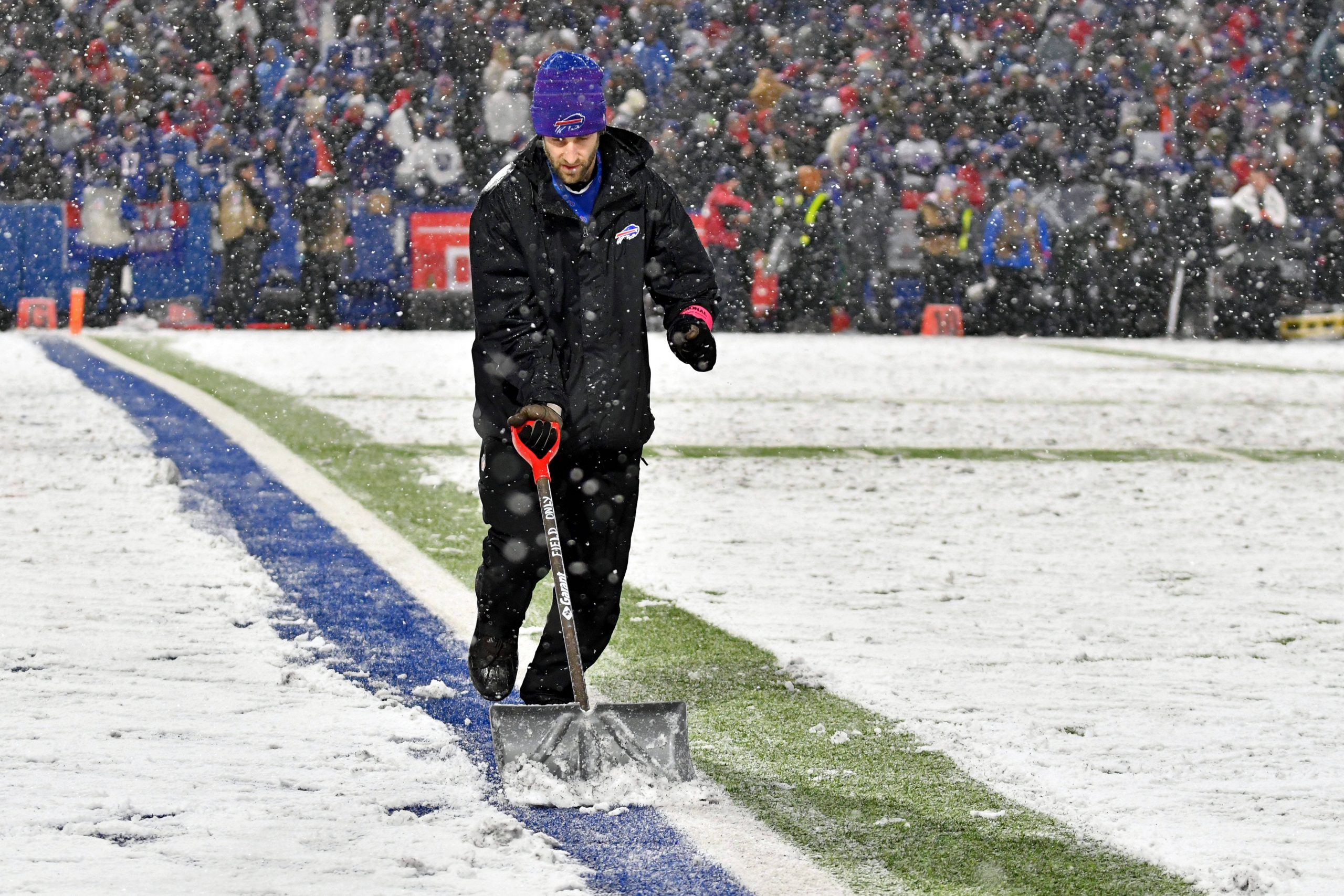 FootballR - NFL - Ein Helfer schaufelt Schnee auf dem Footballplatz im Highmark Stadium.