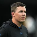FootballR - NFL - Diese Beschreibung wurde automatisch generiert. Kellen Moore, der Offensiv Coordinator der Dallas Cowboys, beobachtet aufmerksam, wie ein Mann in einem schwarzen Kapuzenpullover während eines Eagles-Spiels auf dem Spielfeld steht.