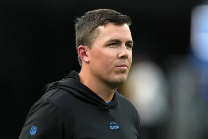 FootballR - NFL - Diese Beschreibung wurde automatisch generiert. Kellen Moore, der Offensiv Coordinator der Dallas Cowboys, beobachtet aufmerksam, wie ein Mann in einem schwarzen Kapuzenpullover während eines Eagles-Spiels auf dem Spielfeld steht.