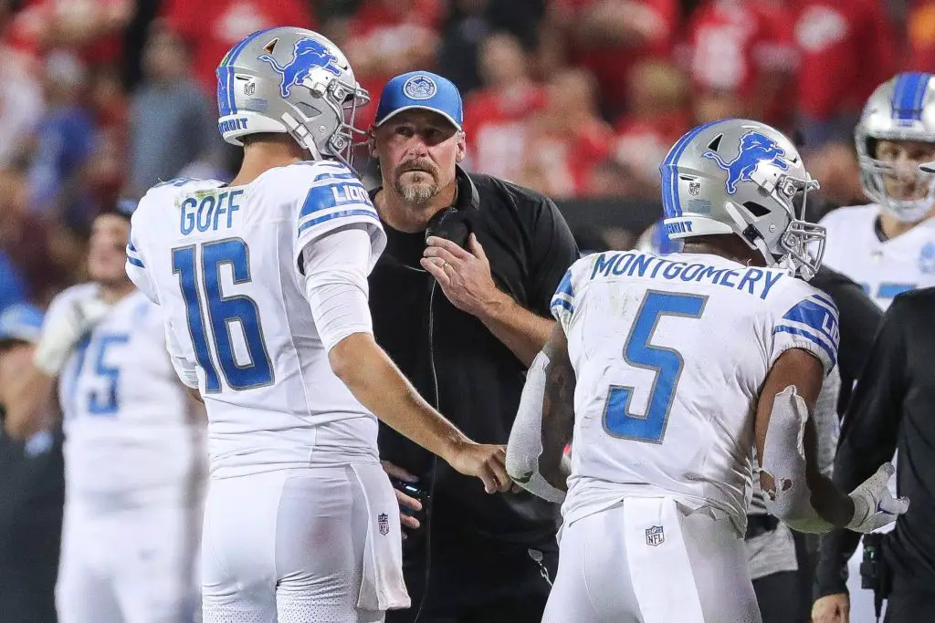 FootballR - NFL - Diese Beschreibung wurde automatisch generiert. Dan Campbell, Cheftrainer der Detroit Lions, spricht während eines Spiels mit seinen Spielern, darunter Jared Goff, und bespricht mit dem Team aggressive Spielstrategien.
