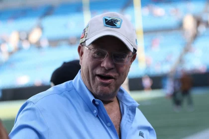 FootballR - NFL - David Tepper, der Besitzer der NFL Carolina Panthers, trägt ein blaues Hemd und eine Mütze und ist auf einem Footballfeld zu sehen.
