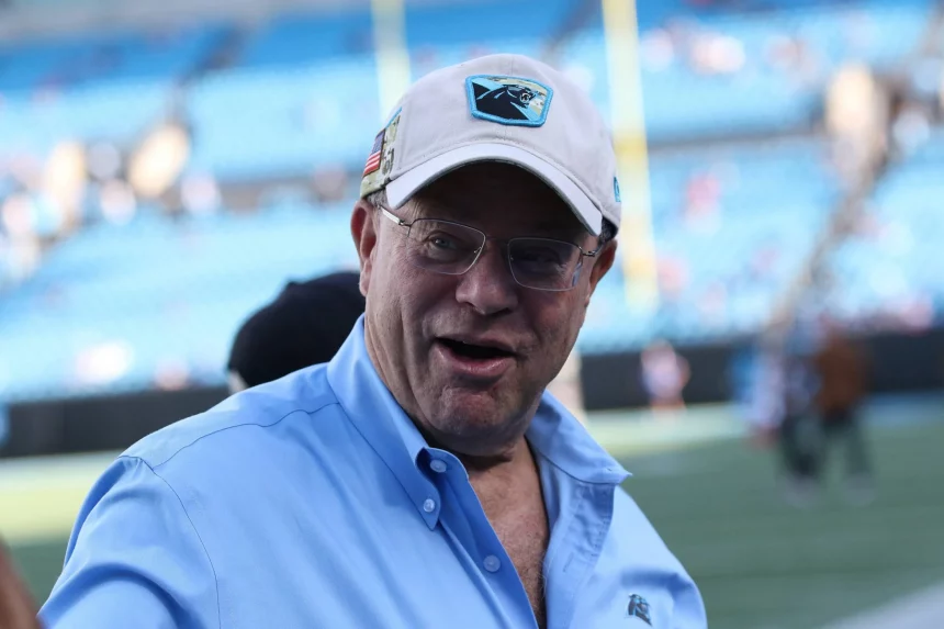 FootballR - NFL - David Tepper, der Besitzer der NFL Carolina Panthers, trägt ein blaues Hemd und eine Mütze und ist auf einem Footballfeld zu sehen.