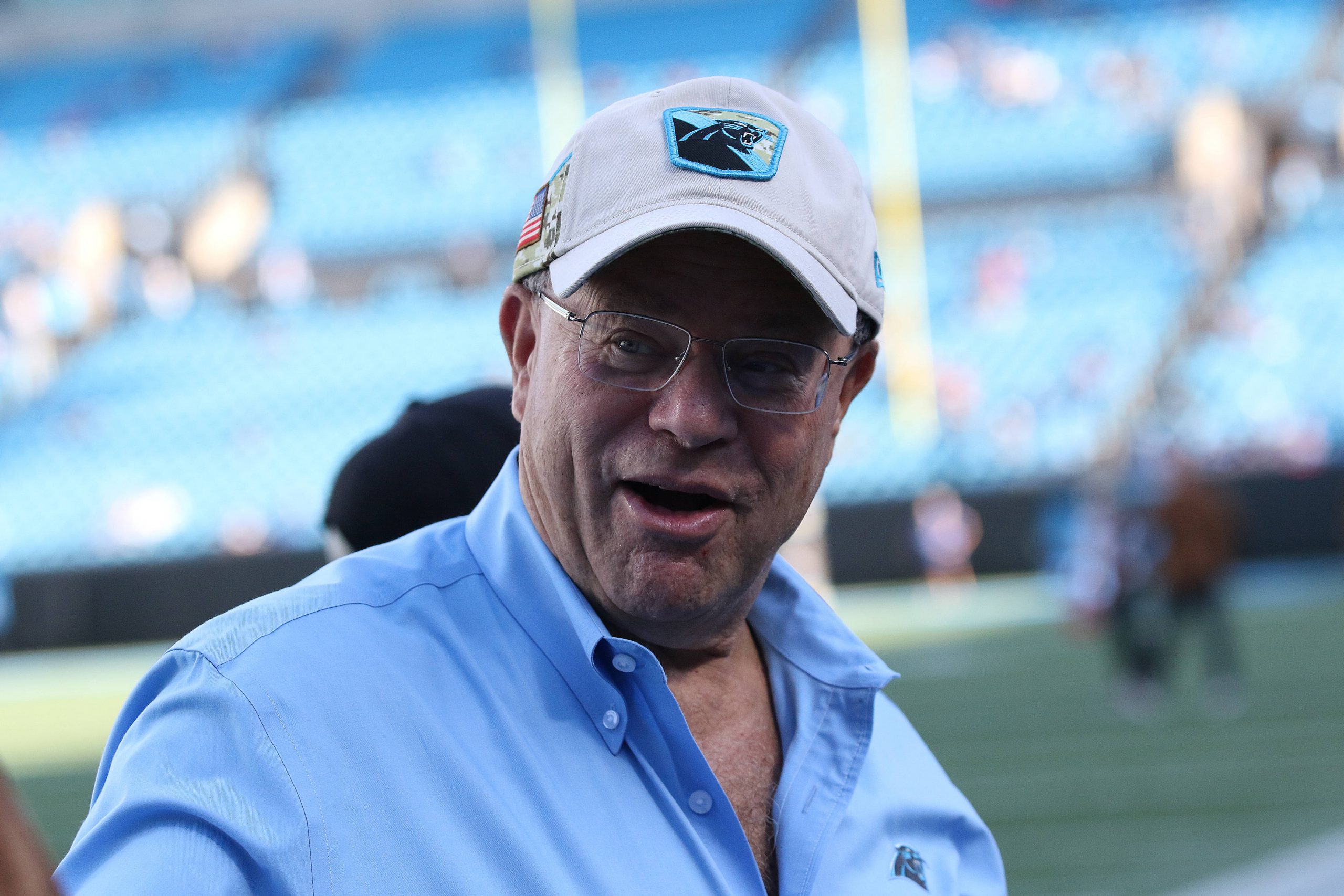 FootballR - NFL - David Tepper, der Besitzer der NFL Panthers, trägt ein blaues Hemd und eine Mütze und ist auf einem Footballfeld zu sehen.