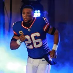 FootballR - NFL - Diese Beschreibung wurde automatisch generiert. Saquon Barkley, ein Running Back der Giants, in blauer Uniform, rennt durch Rauch.