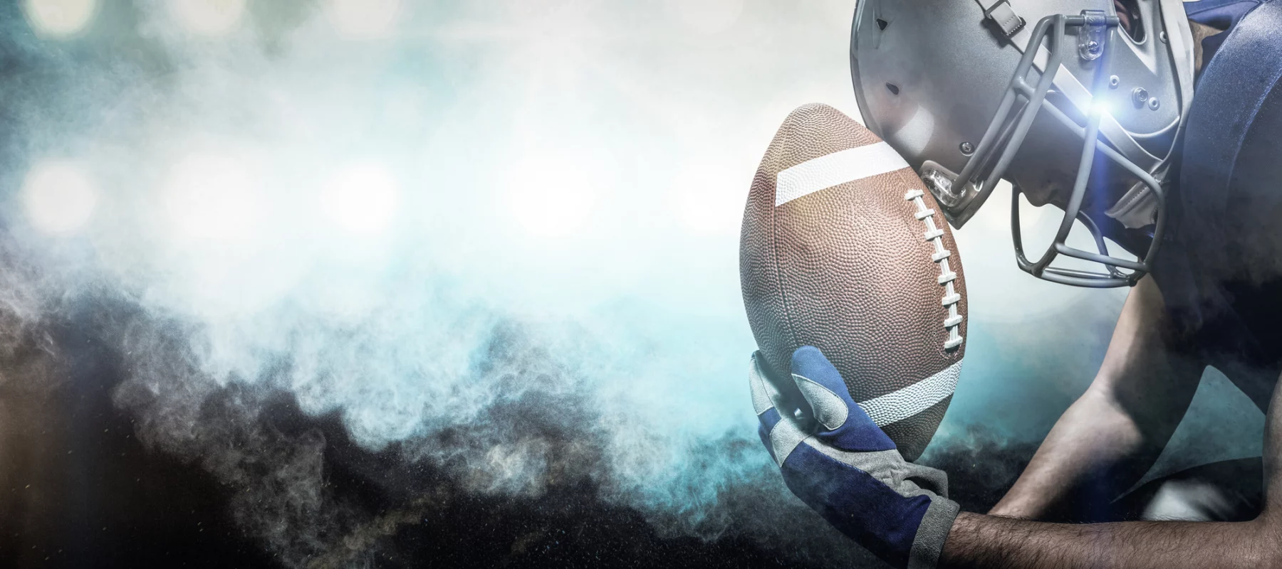 FootballR - NFL - Diese Beschreibung wurde automatisch generiert. Ein Fußballspieler hält einen Ball vor Rauch.