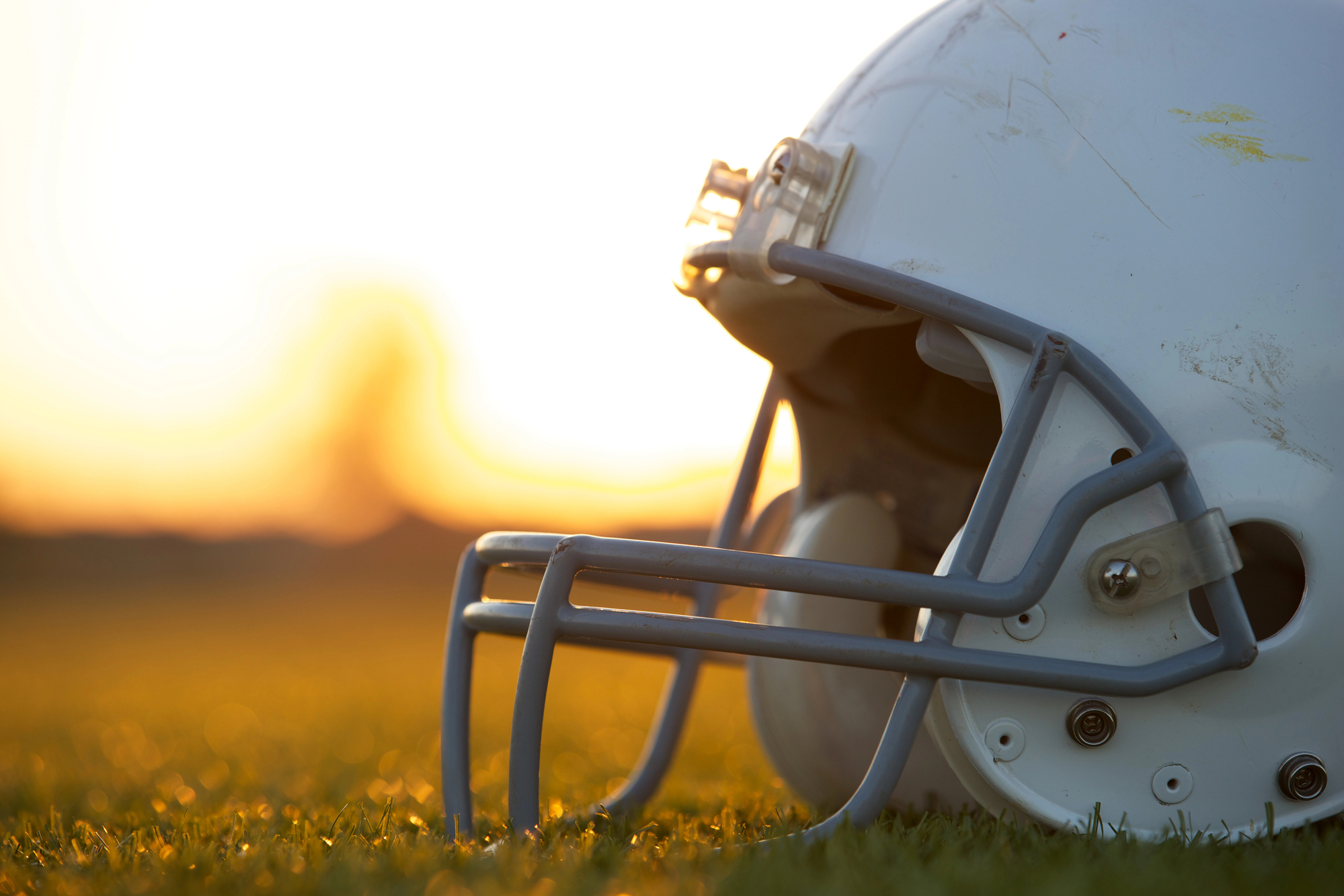 FootballR - NFL - Diese Beschreibung wurde automatisch generiert. Bei Sonnenuntergang sitzt ein weißer Football-Helm auf dem Rasen.