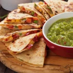FootballR - NFL - Diese Beschreibung wurde automatisch generiert. Quesadillas mit Guacamole auf einem Holzteller.