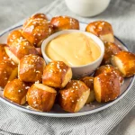 FootballR - NFL - Diese Beschreibung wurde automatisch generiert. Ein Teller mit Mini-Brezelhäppchen mit Käsefüllung und Senf darauf.