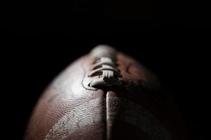 FootballR - NFL Franchise Tag - Diese Beschreibung wurde automatisch generiert. Eine Nahaufnahme, die einen Football vor einem schwarzen online Casinos Hintergrund zeigt.