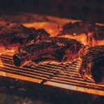 FootballR - NFL - Diese Beschreibung wurde automatisch generiert. Fleisch auf einem Grill mit Flammen.