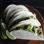 FootballR - NFL - Diese Beschreibung wurde automatisch generiert. Vier Tacos auf einem Holzteller mit Limettenspalten.