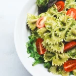 FootballR - NFL - Diese Beschreibung wurde automatisch generiert. Pesto-Nudelsalat auf einem weißen Teller.