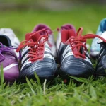 FootballR - NFL - Diese Beschreibung wurde automatisch generiert. Eine Gruppe Sportschuhe steht aufgereiht auf dem Rasen.