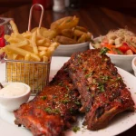 FootballR - NFL - Diese Beschreibung wurde automatisch generiert. Glasierte Rippchen und eine Beilage Pommes und Salat auf einem Tisch.