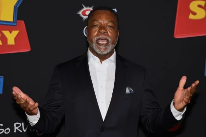 FootballR - NFL - Diese Beschreibung wurde automatisch generiert. Ein Hollywood-NFL-Spieler, Carl Weathers, in einem Anzug mit erhobenen Händen.