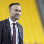 FootballR - NFL - Diese Beschreibung wurde automatisch generiert. Jeff Hafley, ein Mann in Anzug und Krawatte, steht in einem Stadion.